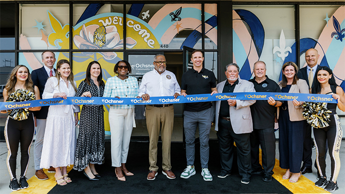 Group of people, including a Congressman holding a ribbon with the Ochsner Health logo on it outdoors in front of a Ochsner Health property.